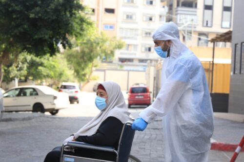 A healthcare worker in Gaza seen helping a Palestinian lady on a wheelchair