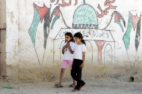 Two girls walk past a graffiti-strewn wall in the United Nations Relief and Works Agency for Palestine Refugees in the Near East (UNRWA)'s Acqba Jaber camp for Palestinian refugees, in the West Bank, located just outside of Jericho [UN Photo/Stephenie Hollyman]